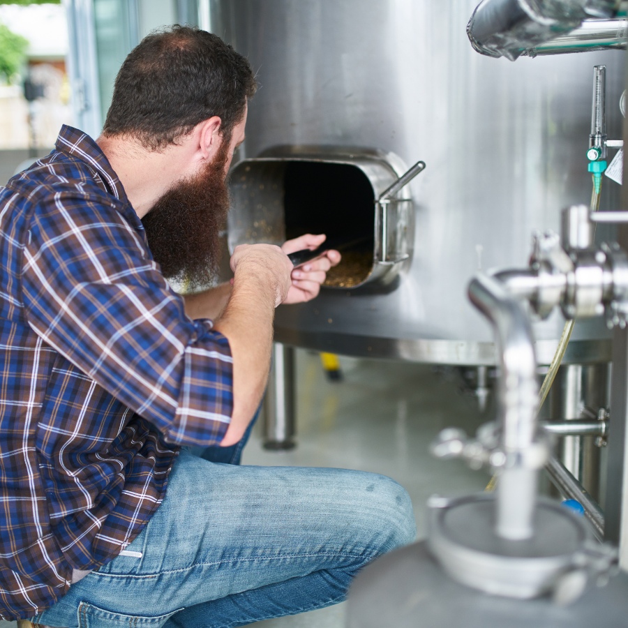 A man in a plaid shirt kneeling down and cleaning the inside of a brewery vat.